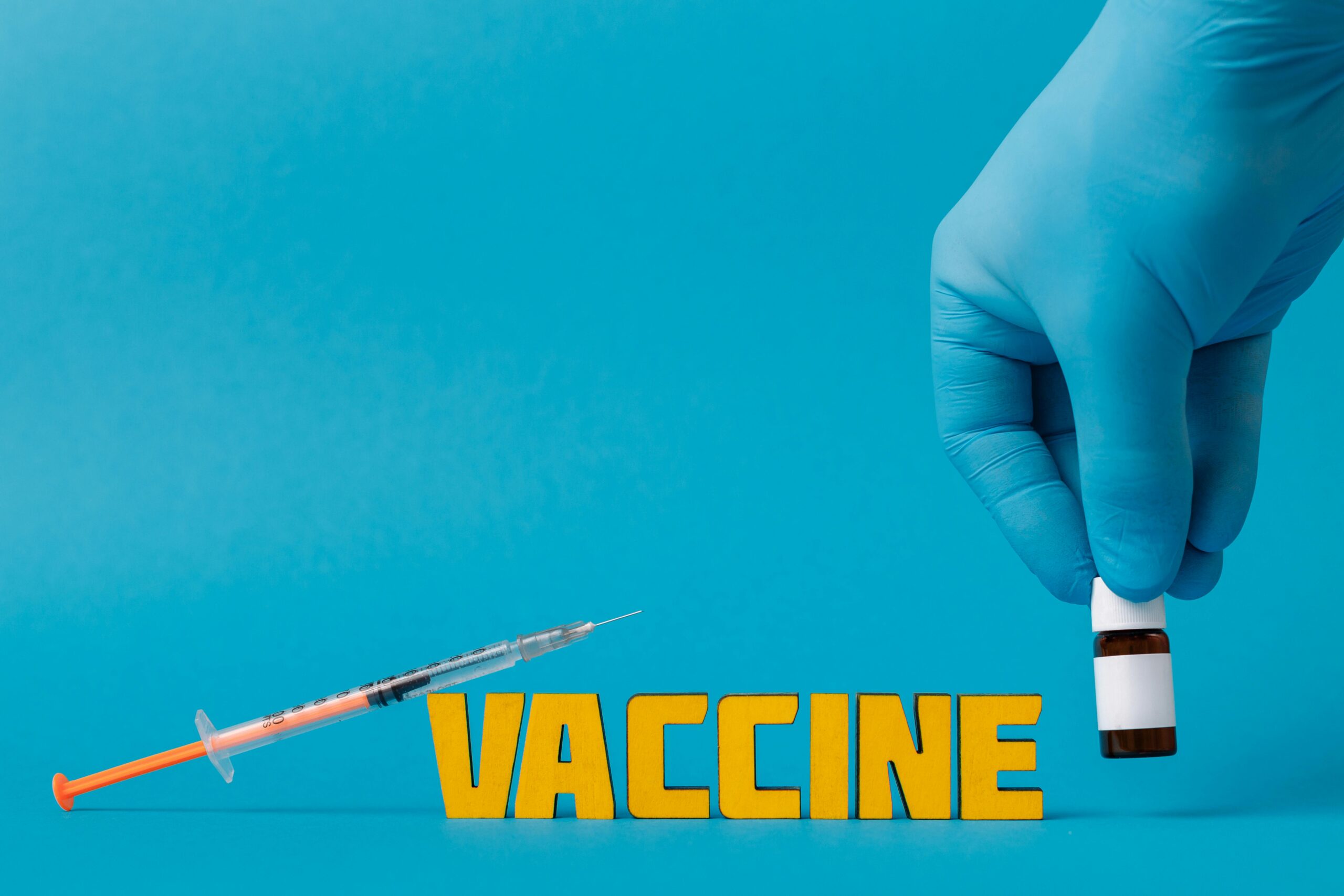 Medical concept with syringe and vaccine bottle against blue background featuring yellow text "VACCINE".